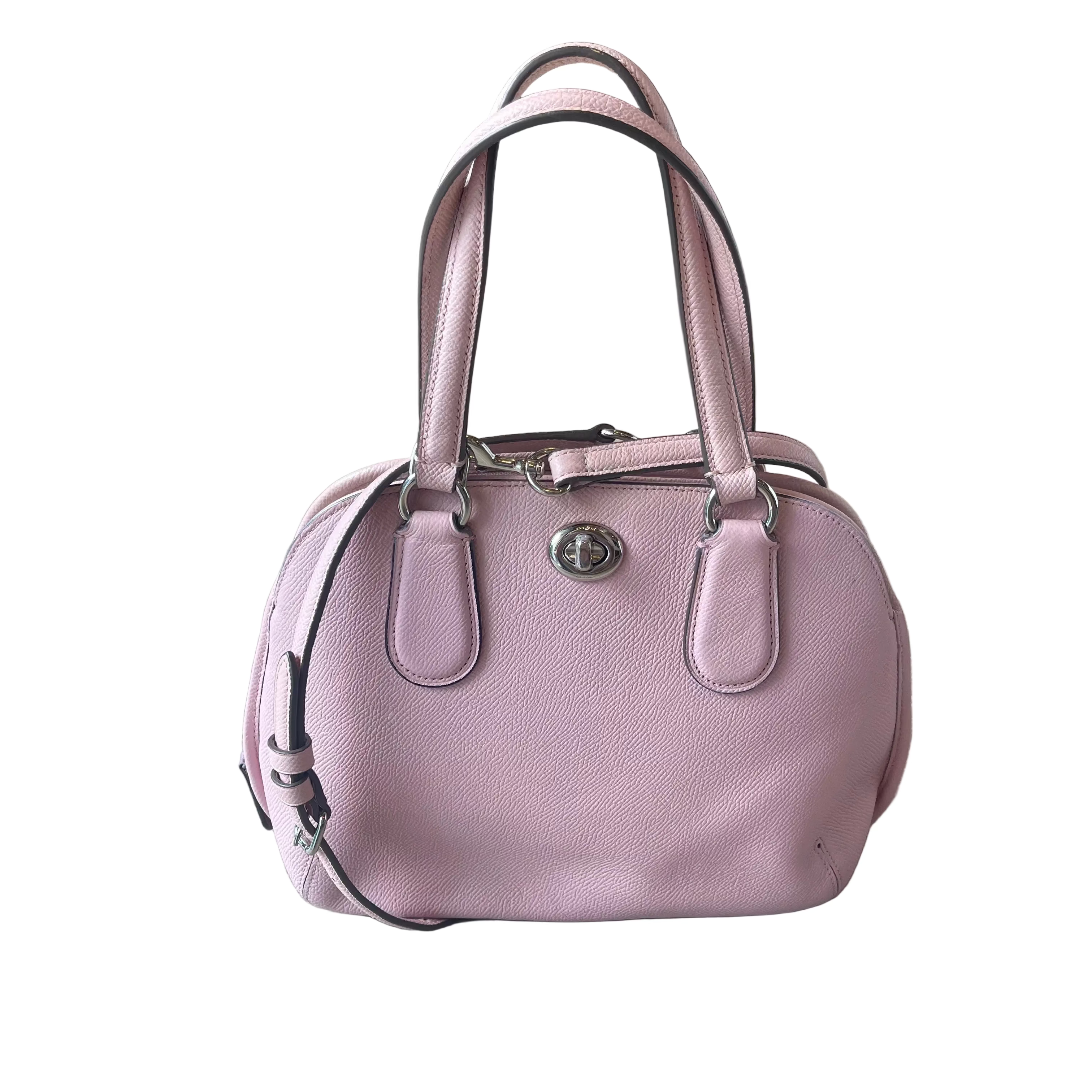 A dusty pink pebbled leather handbag with double top handles and silver-tone hardware, resting on a light wood floor.