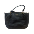 A black pebbled leather Coach handbag with gold-tone hardware and a top handle, laid flat on a white textured fabric background.