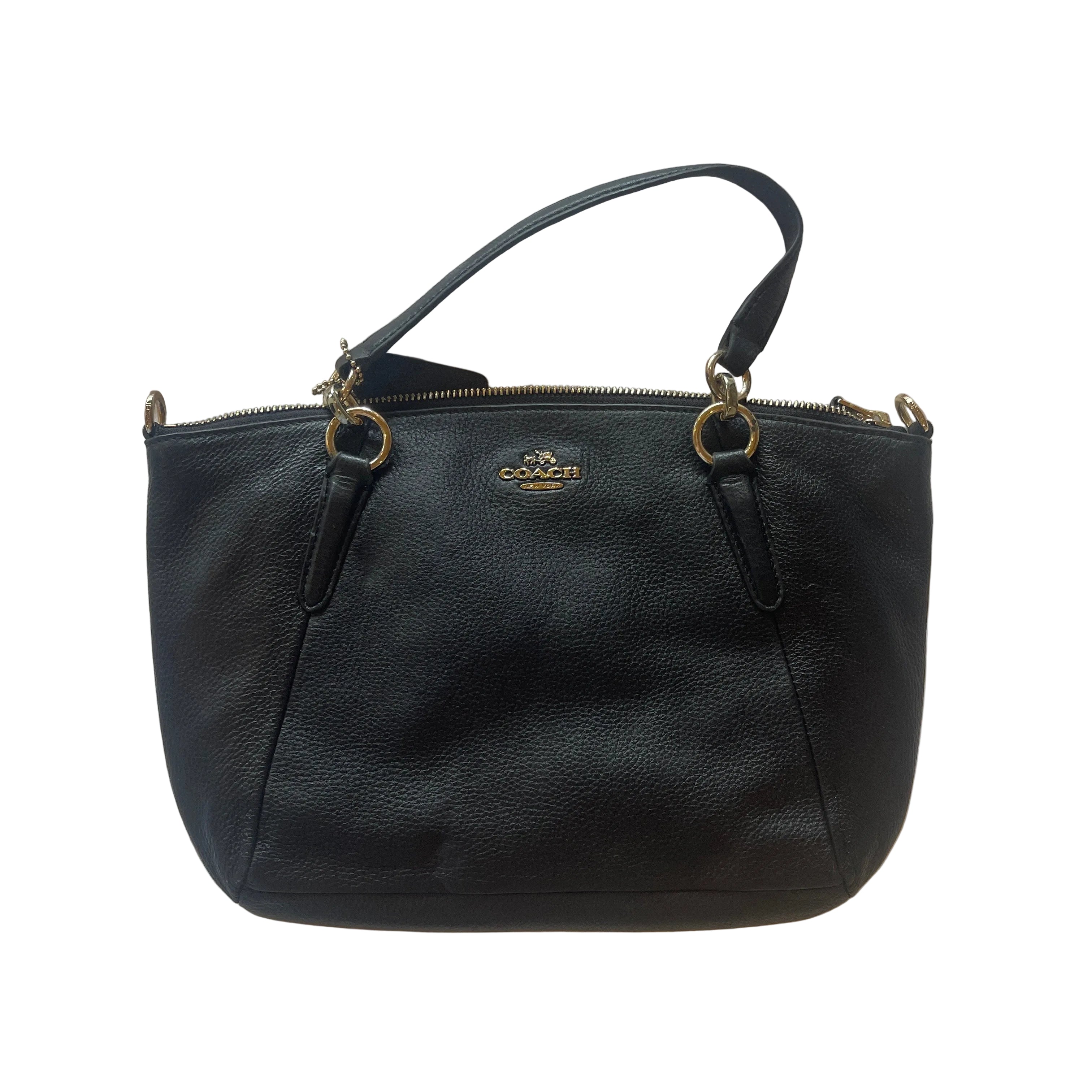 A black pebbled leather Coach handbag with gold-tone hardware and a top handle, laid flat on a white textured fabric background.