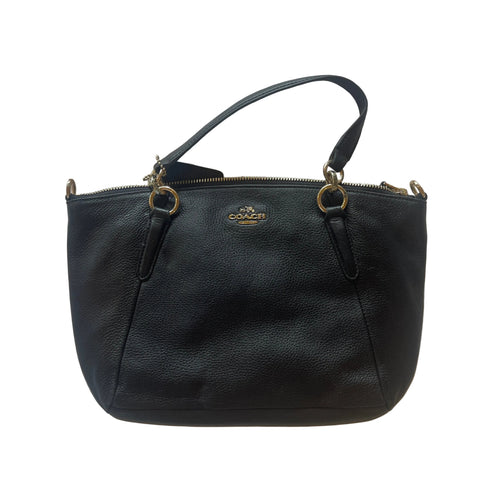 A black pebbled leather Coach handbag with gold-tone hardware and a top handle, laid flat on a white textured fabric background.